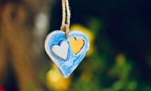 Hand-painted blue clay ornament, shaped like a heart with heart cut-out and carved heart outline in center of the ornament 